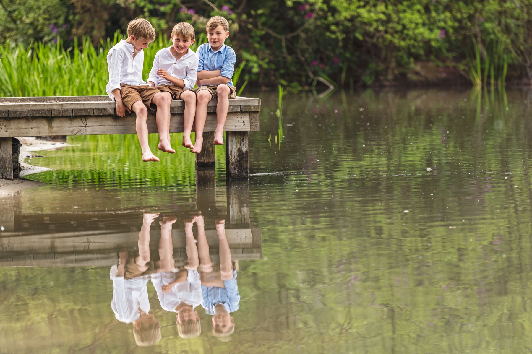 Three children sitting by a lake with reflections in the water